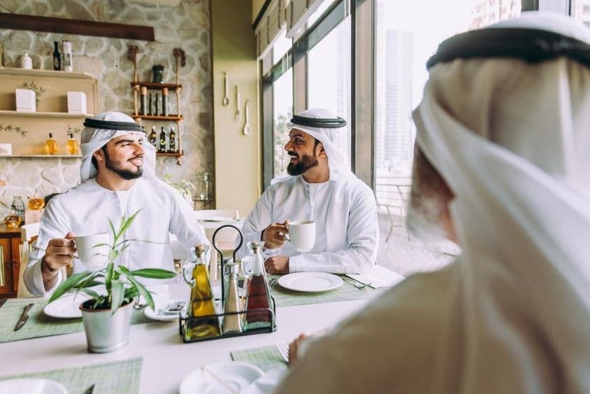 Drei Geschäftsleute trinken Tee in Dubai, in traditioneller Emirati-Tracht.