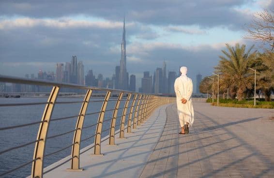 Emirati-Mann, der auf einem Bürgersteig mit dem Burj Khalifa im Hintergrund geht.