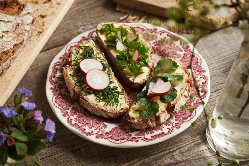 Essbare Pflanzen - Schnittlauch, Knoblauchrauke und Stachelbeeren auf gebutterten Sauerteigschnitten.