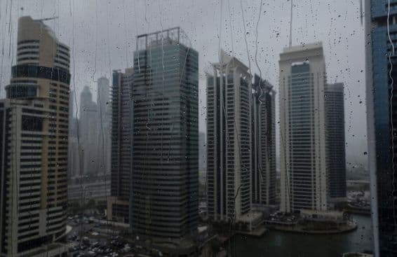Nahaufnahme eines nassen Fensters mit der modernen Skyline von Dubai im Hintergrund.