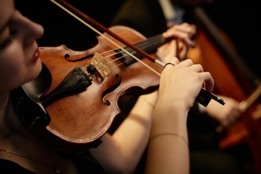 Weibliche Orchestermusikerin spielt während eines Bühnenkonzerts Geige mit Bogen.