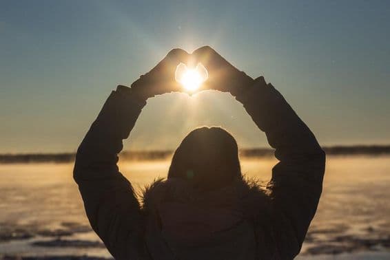 Frau formt Herzen mit ihren Händen bei frostigem Sonnenuntergang im Freien.
