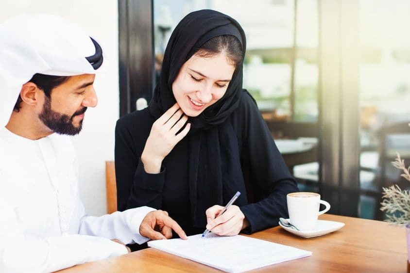 Arabischer Mann reicht einer Frau im Hijab Dokumente zum Unterschreiben.