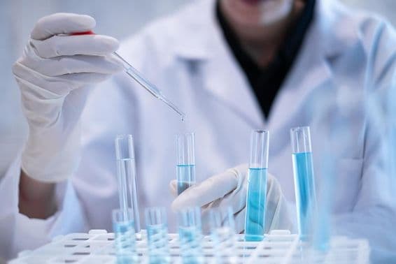 Wissenschaftler pipettiert blaue Flüssigkeit in ein Reagenzglas im Labor.