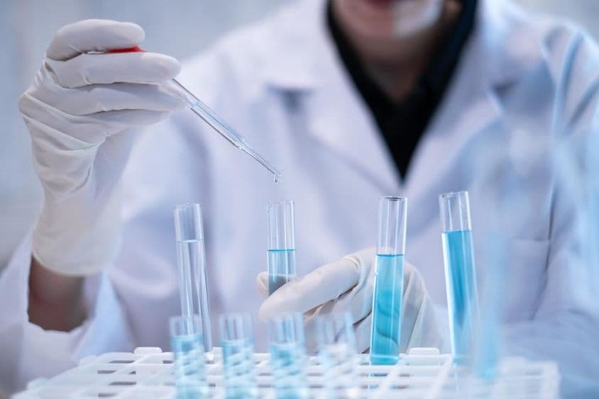 Wissenschaftler pipettiert blaue Flüssigkeit in ein Reagenzglas im Labor.