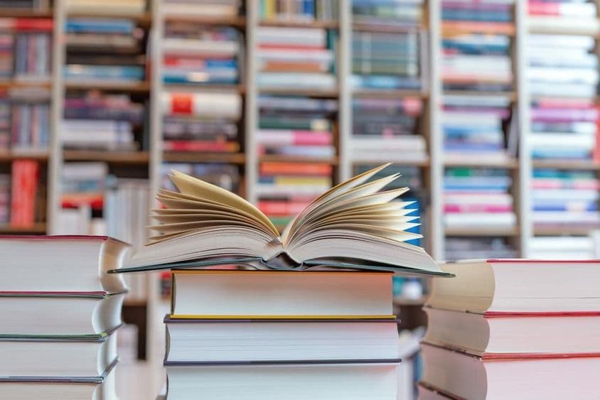 Aufgeschlagenes Buch auf einem Bücherstapel vor einem Regal.
