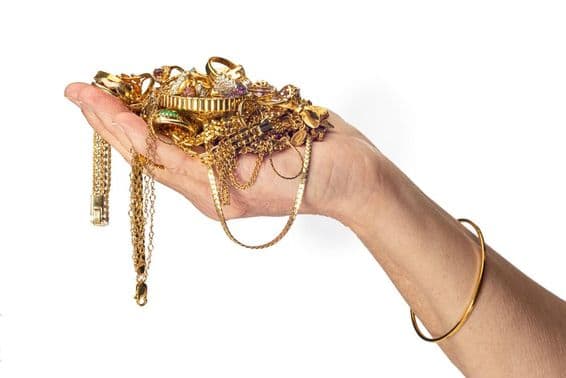 Eine Frauenhand hält einen Haufen Goldschmuck und trägt ein Armband.