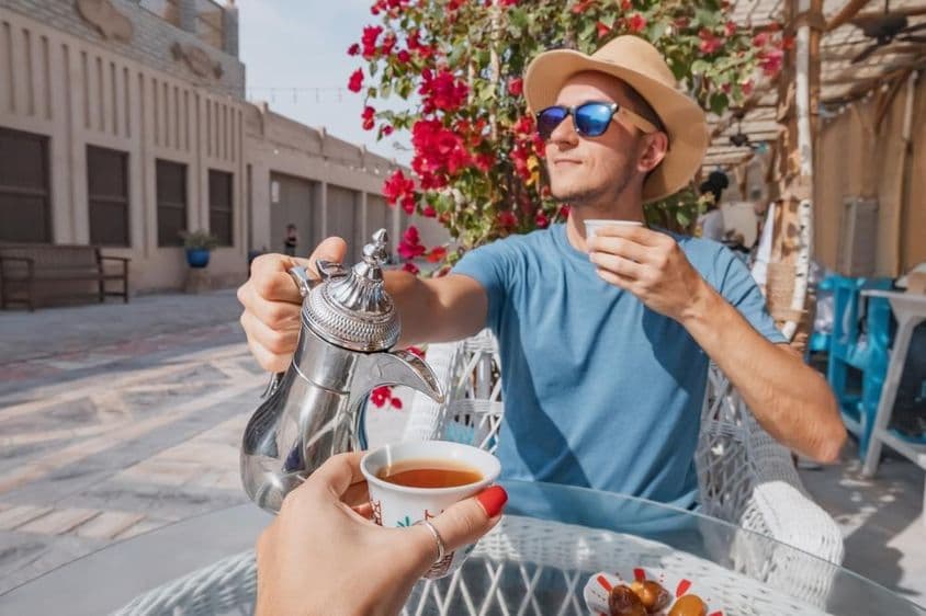 Ein Mann in Dubai ruht sich in einem arabischen Café aus und gießt aromatischen Kaffee aus einer Dallah-Kaffeekanne ein.