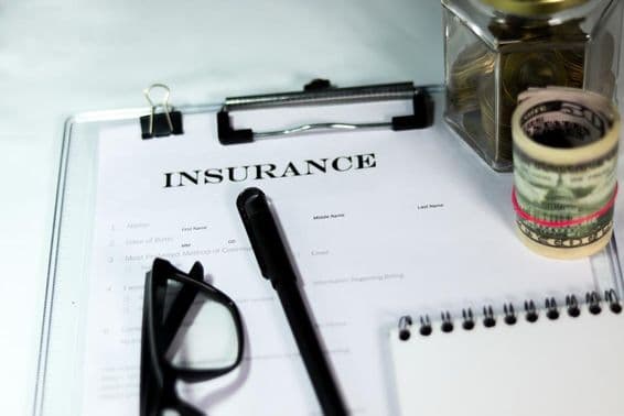 Versicherungsformular mit Münzbox, Dollarpaket, Stift und Brille.