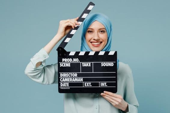 Junge arabische muslimische Frau in Abaya-Hijab hält eine klassische schwarze Filmklappe.