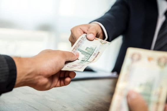 Geschäftsmann, der Geld in VAE-Dirham-Währung an einen Partner übergibt.