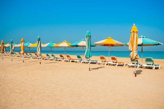 Öffentlicher Strand in Dubai, Sandküste, Sonnenliegen und blaues Meer.