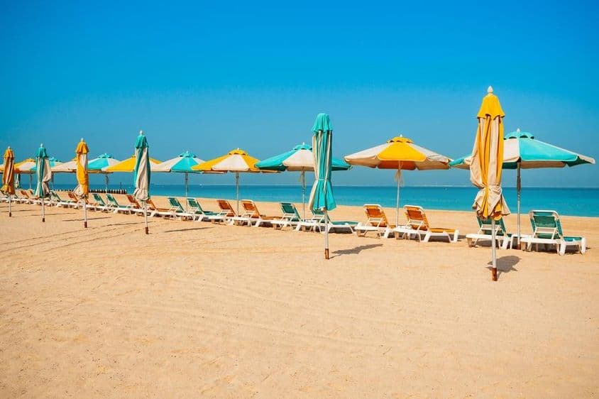 Öffentlicher Strand in Dubai, Sandküste, Sonnenliegen und blaues Meer.