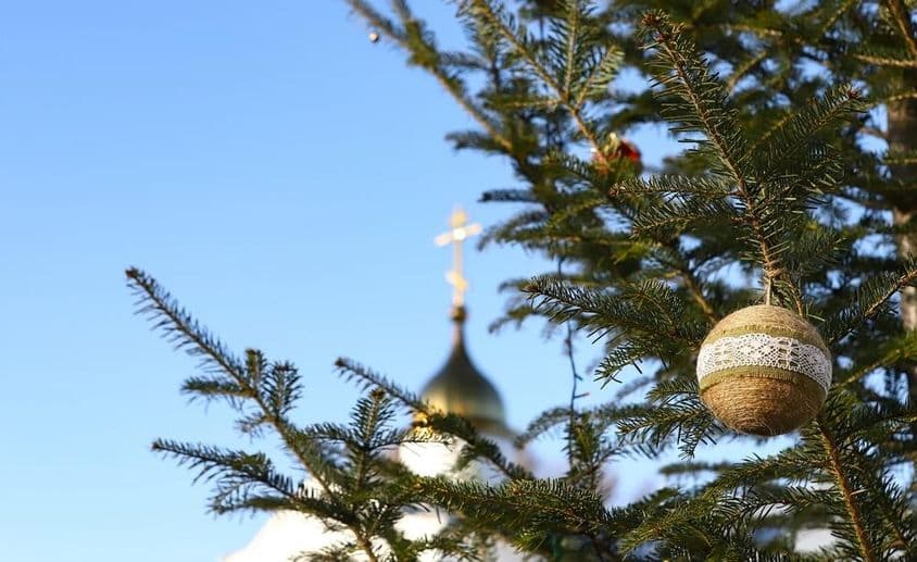 Zweig eines Weihnachtsbaums mit Ornamenten, mit einem orthodoxen Kreuz im Hintergrund.