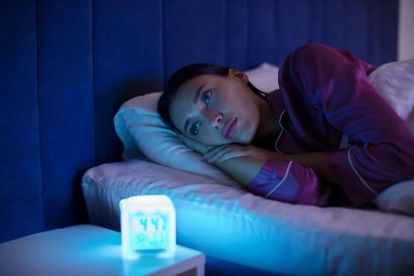 Traurige schlaflose Frau liegt im Bett, starrt weg und leidet unter Schlaflosigkeit.