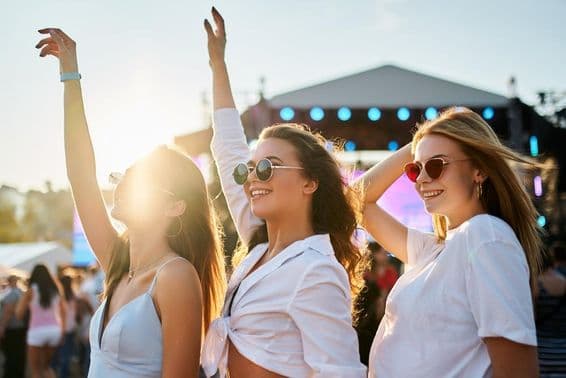 Mädchen in Sommerkleidern genießen ein Konzert und feiern mit erhobenen Händen.