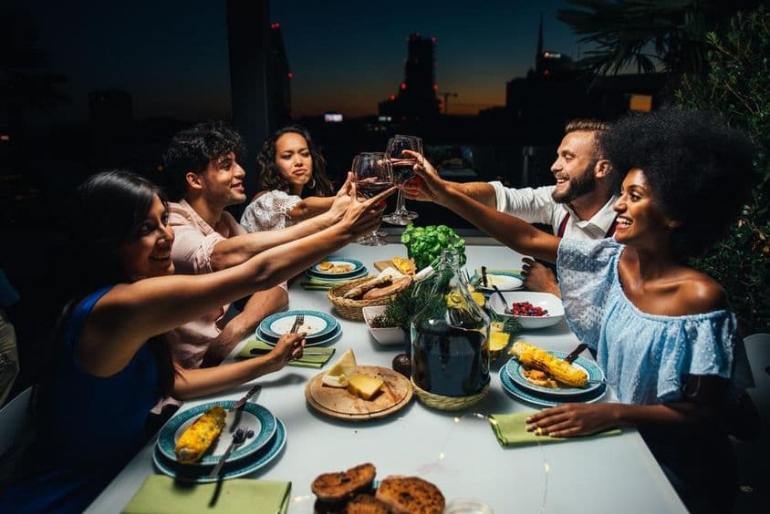 Gruppe von Freunden genießt eine Mahlzeit und feiert auf einem schönen Penthouse-Balkon.