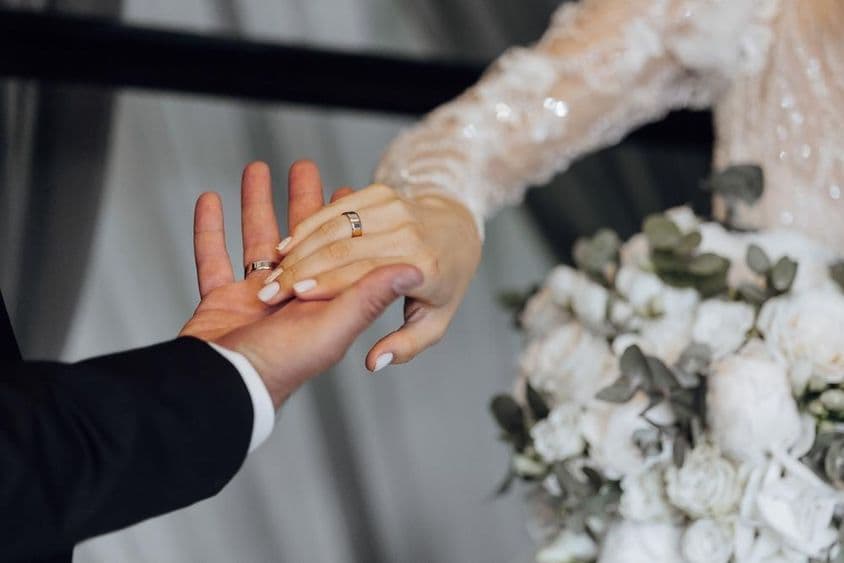 Braut und Bräutigam halten sich an den Händen, Braut trägt ein weißes Kleid.