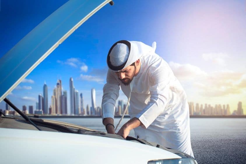 Ein arabischer Mann inspiziert sein Auto, die Motorhaube ist geöffnet.