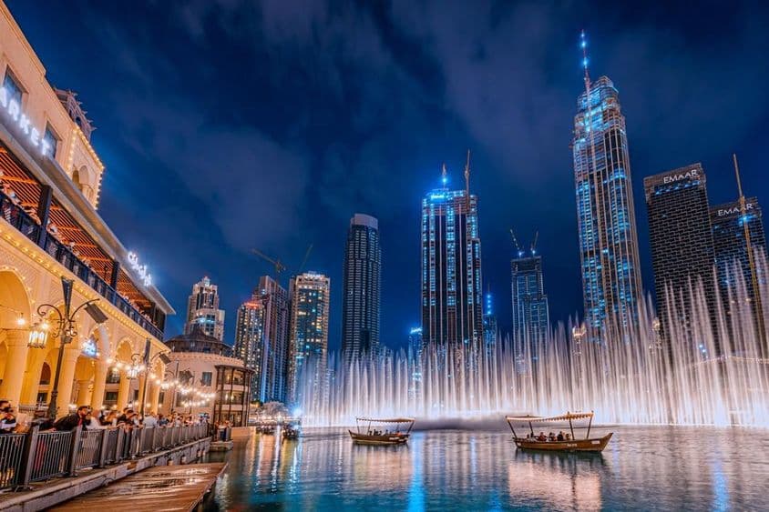 Personen im Boot, die nachts die Dubai-Fontäne mit Dubais Wolkenkratzern im Hintergrund beobachten.