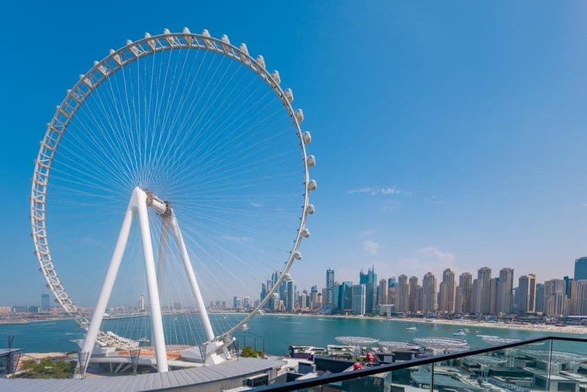 Riesenrad Ain Dubai mit Wolkenkratzern und Meer im Hintergrund.