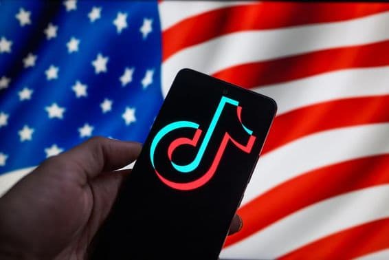 Das TikTok-Logo auf einem Smartphone mit der amerikanischen Flagge im Hintergrund.