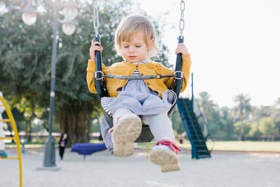 Glückliches Kleinkindmädchen schaukelt im Park im Sonnenschein.