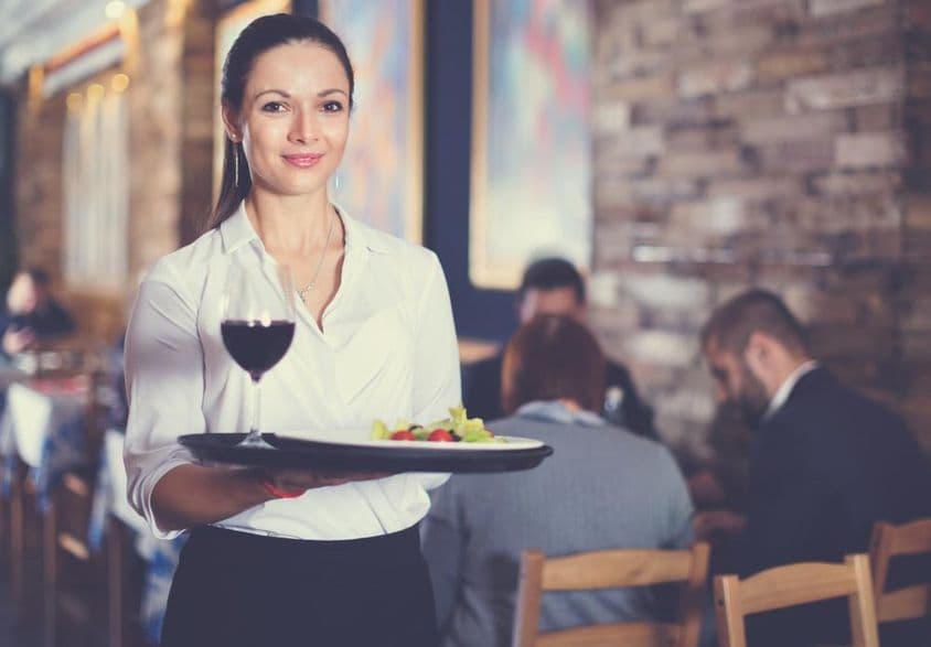 Fröhliche Kellnerin mit Serviertablett für Restaurantgäste.