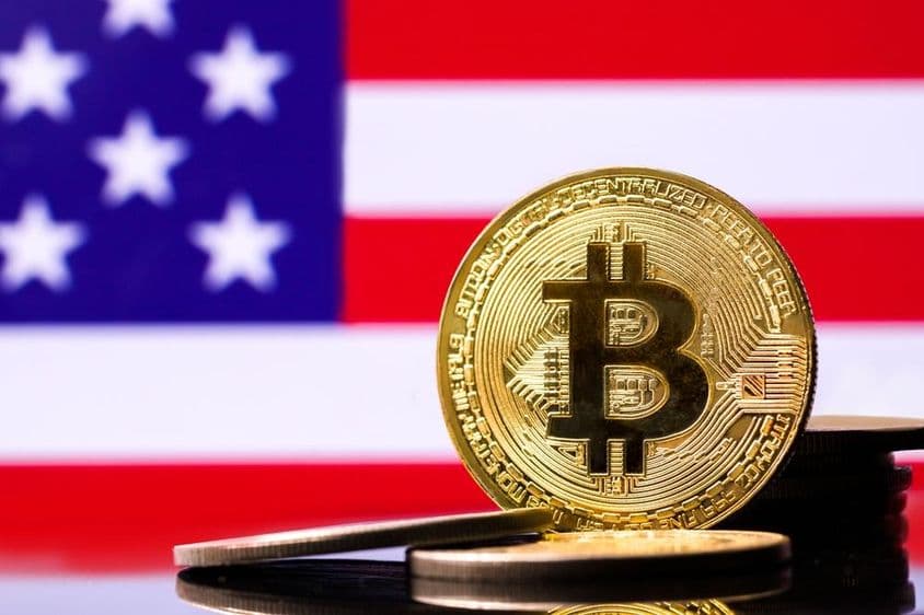 Goldene Bitcoin-Münze mit der US-Flagge im Hintergrund.