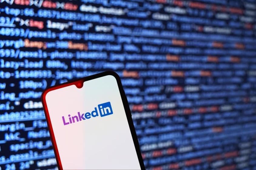 Smartphone mit LinkedIn-Logo und Codeschnipsel im Hintergrund.