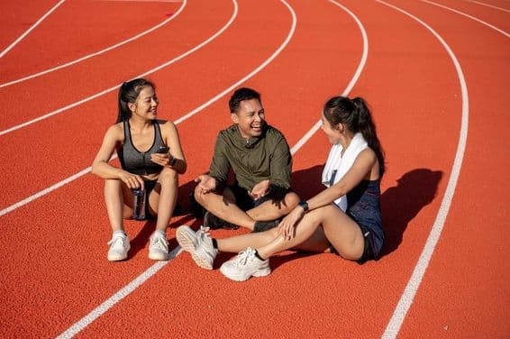 Eine Gruppe fröhlicher Athletinnen, die sich nach dem Training unter der Sonne auf einem Sportfeld ausruhen.