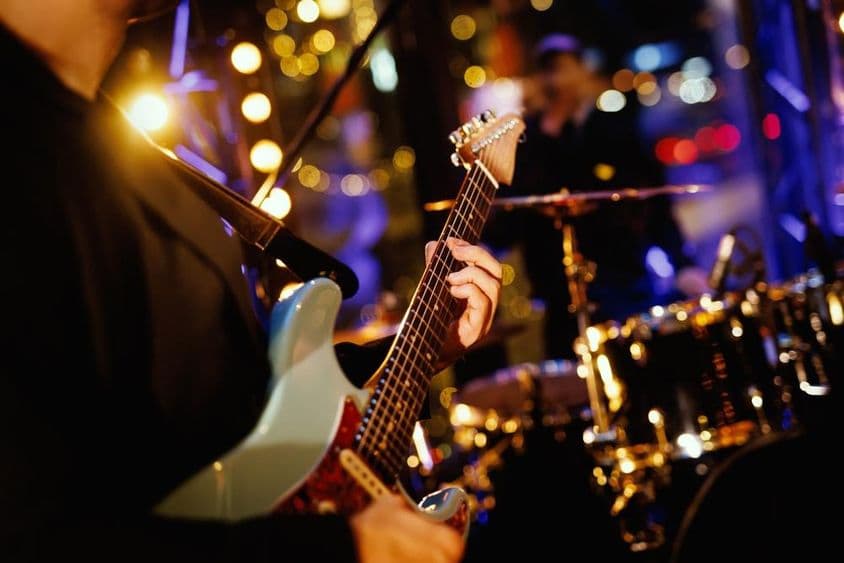 Ein Gitarrist spielt einen Akkord auf dem Griffbrett während eines Bandauftritts.