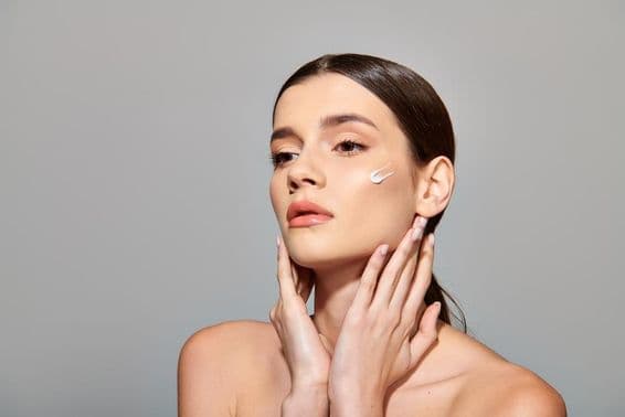 Eine junge Frau mit braunen Haaren trägt eine Schönheitscreme auf ihr Gesicht auf und strahlt ein Gefühl von Selbstfürsorge aus.