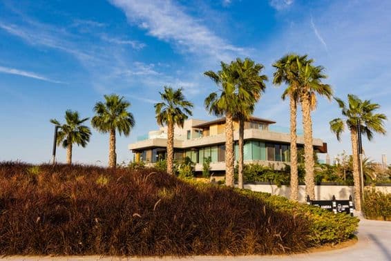 Dubai, Villa umgeben von Palmen vor bewölktem Sonnenuntergang.