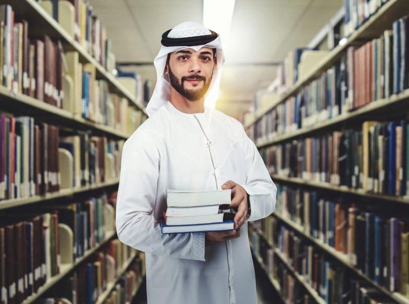 Arabischer Student steht in der Bibliothek und hält Bücher.
