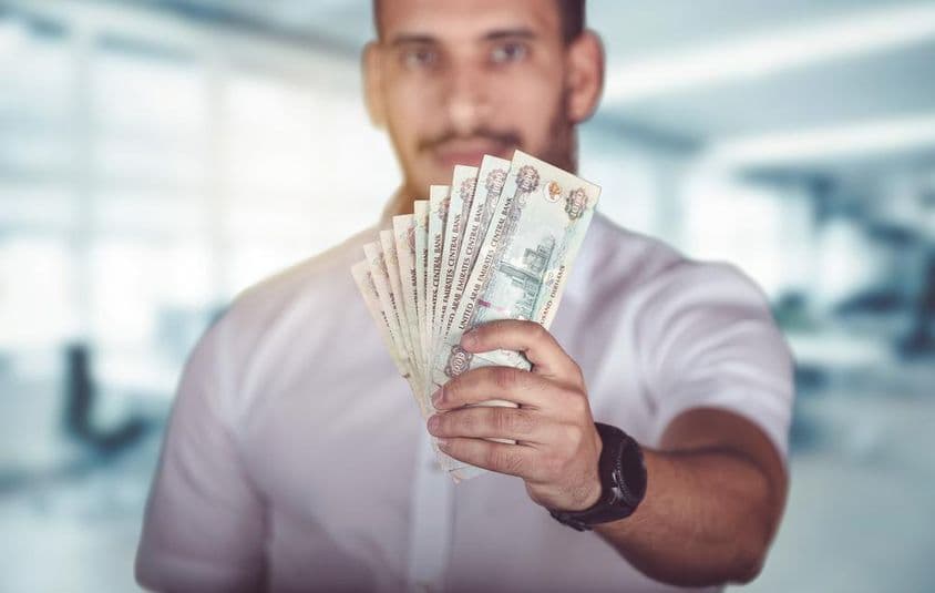 Mann hält eine Handvoll Emirati-Dirham-Bargeld.