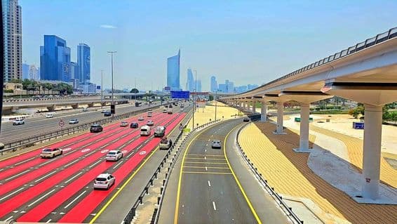 In Dubai ist die Straße rot bemalt mit weißen Fahrbahnmarkierungen und Geschwindigkeitsbegrenzungsschildern, die 100 km/h anzeigen.
