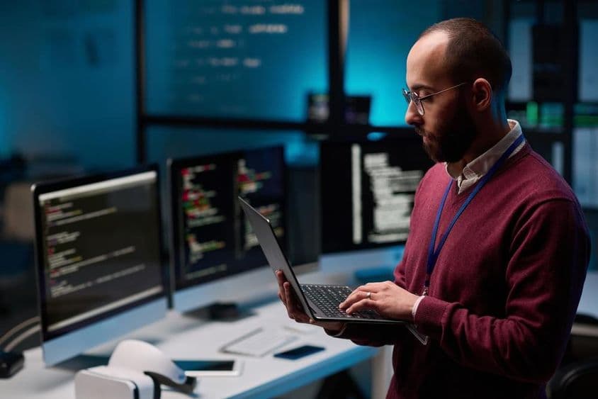 Computerprogrammierer hält einen offenen Laptop in einem IT- und Cyber-Sicherheitsbüro.