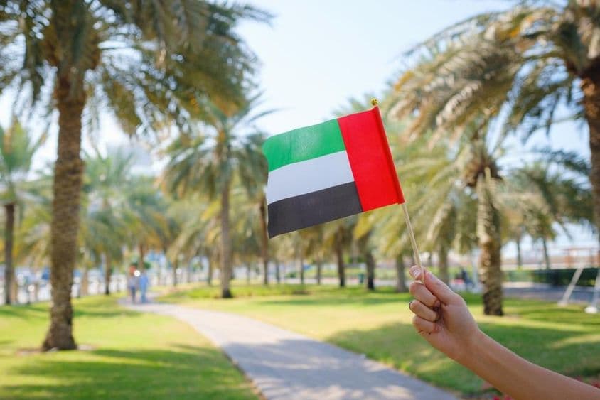 Eine Frauenhand hält eine Miniaturflagge der Vereinigten Arabischen Emirate in einem Park in Abu Dhabi.