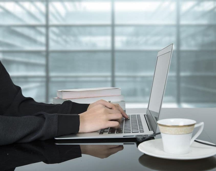 Eine Frau arbeitet an einem Laptop mit einer Kaffeetasse daneben.
