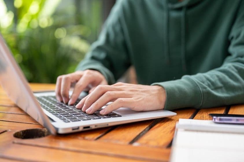 Mann in grünem Pullover arbeitet draußen an einem Laptop.