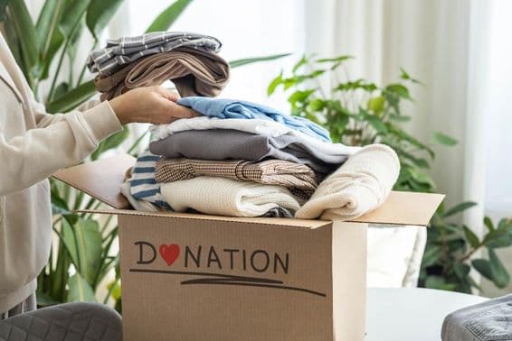 Eine Frau zu Hause, die Kleidung in einen Karton für Spenden, zum Recycling legt.