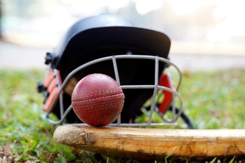 Cricket-Ausrüstung mit Cricketball, Schläger und Helm auf Gras.