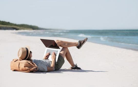 Junge Frau arbeitet am Laptop am Meer und macht Freiberuflerarbeit.