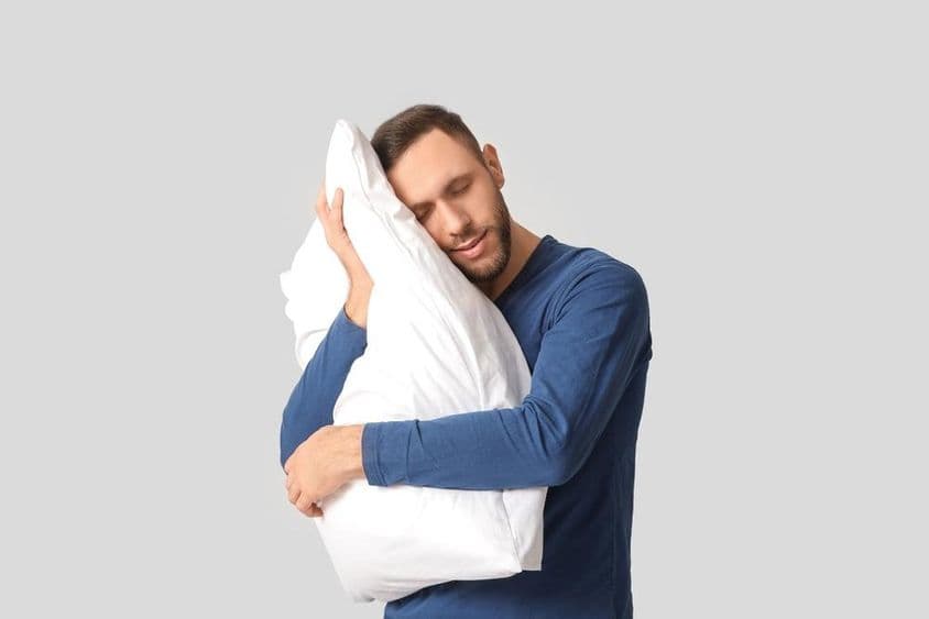 Junger Mann im Pyjama mit weichem Kissen.