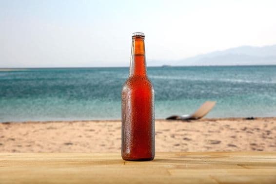 Eine Flasche kaltes Bier auf einem Holztisch am sandigen Strandufer.