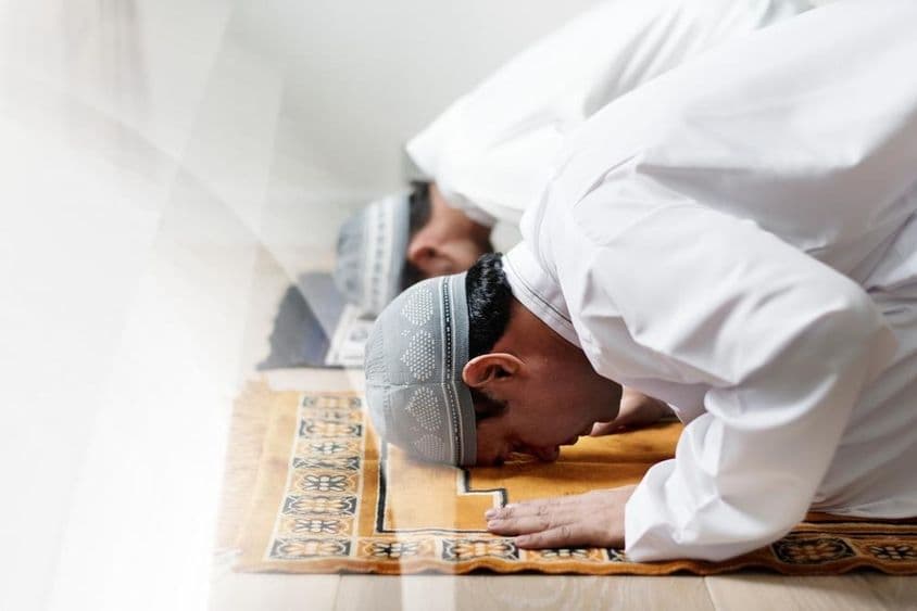 Islamische Männer in Weiß, die im Gebet niederknien.
