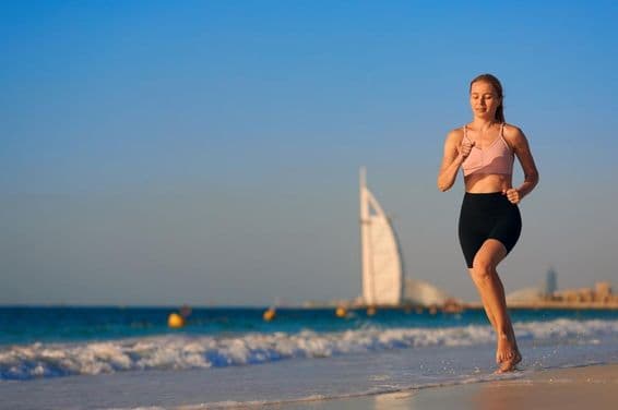 Junge Frau läuft am Strand in Dubai mit Burj Al Arab Jumeirah im Hintergrund.