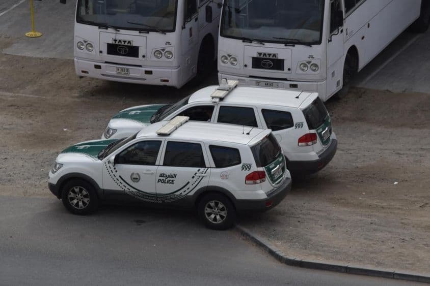 Zwei Dubai Polizeiautos parken vor zwei Bussen in Al Quoz, Dubai.