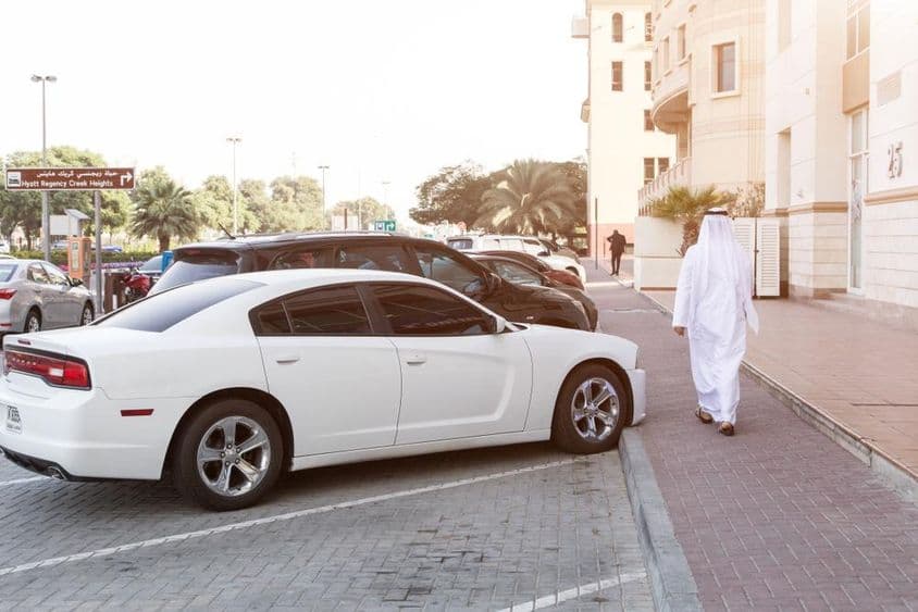 In den Straßen von Dubai: Ein Mann in Nationaltracht und ein weißer Dodge auf dem Parkplatz.